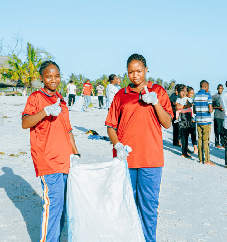 Two volunteers in gloves holding a bag of collected litter on a beach