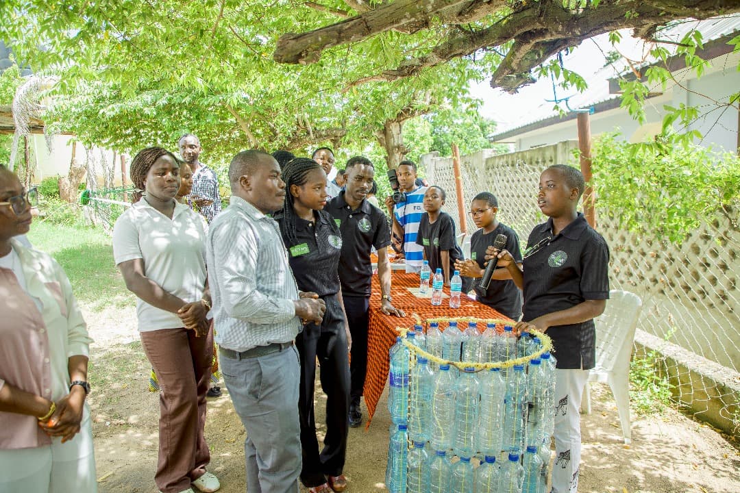 A student presenting a structure made of plastic bottles to a group of adults